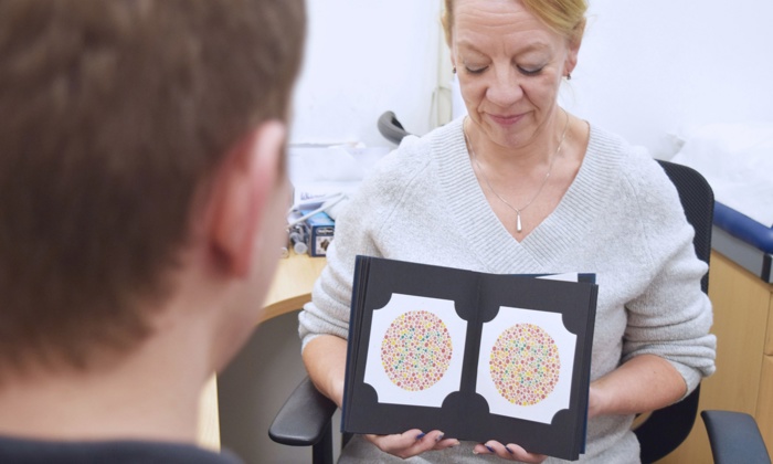 A woman sits in an office holding and looking at a book with two colored dot patterns, facing a person sitting across from her.