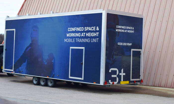 A mobile training unit trailer for confined space and working at height is strategically parked outside a large building, ready to provide essential safety training.
