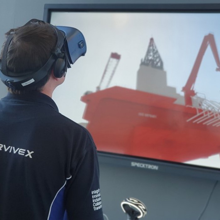 Uma pessoa com um auricular de realidade virtual interage com uma simulação virtual de uma plataforma offshore apresentada num ecrã de grandes dimensões.