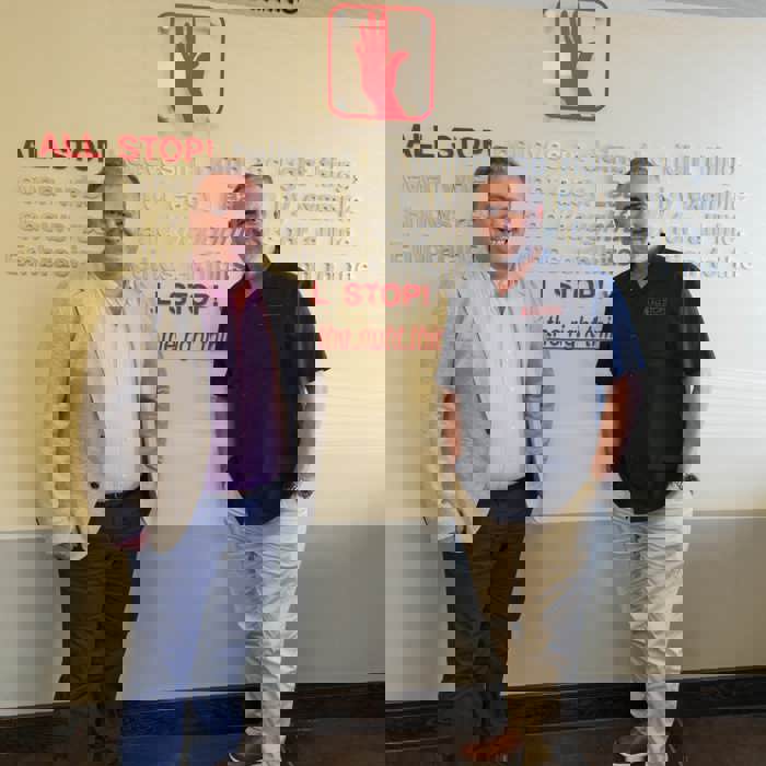 Deux hommes se tiennent avec assurance devant un mur orné du texte "ALL STOP ! Survival & Safety Training". L'un porte un blazer impeccable tandis que l'autre opte pour une chemise noire élégante, incarnant l'essence même de la préparation d'une formation professionnelle.