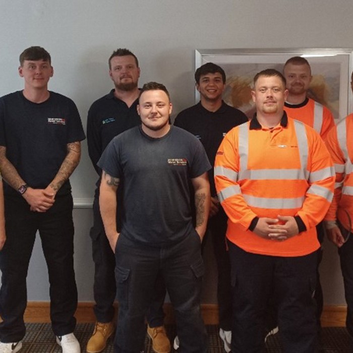 Huit hommes se tiennent à l'intérieur, certains en uniforme de travail, peut-être réunis pour une séance d'entraînement.