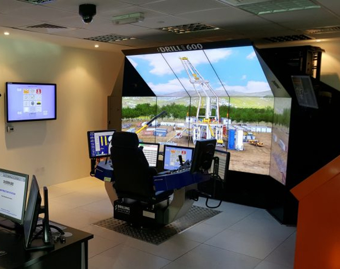 A modern drilling simulator setup with multiple screens showing an outdoor drilling scenario. The control console is equipped with joysticks and monitors displaying various operational data.