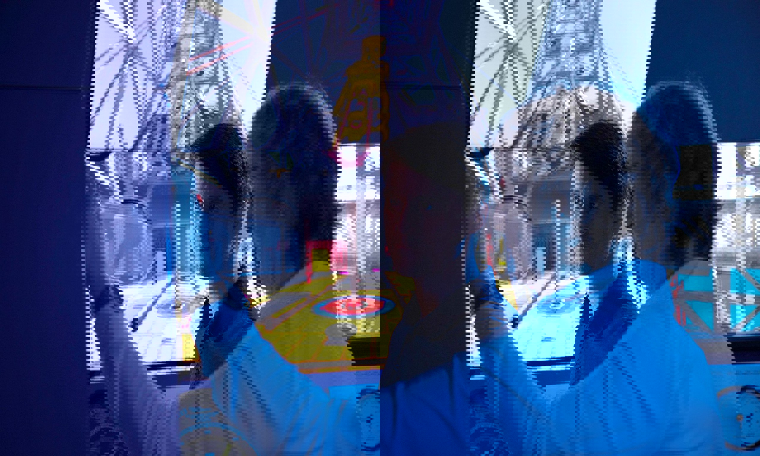 Two men in a control room operate a simulator with a large screen displaying the interior of an industrial setting. One is pointing while the other observes intently.