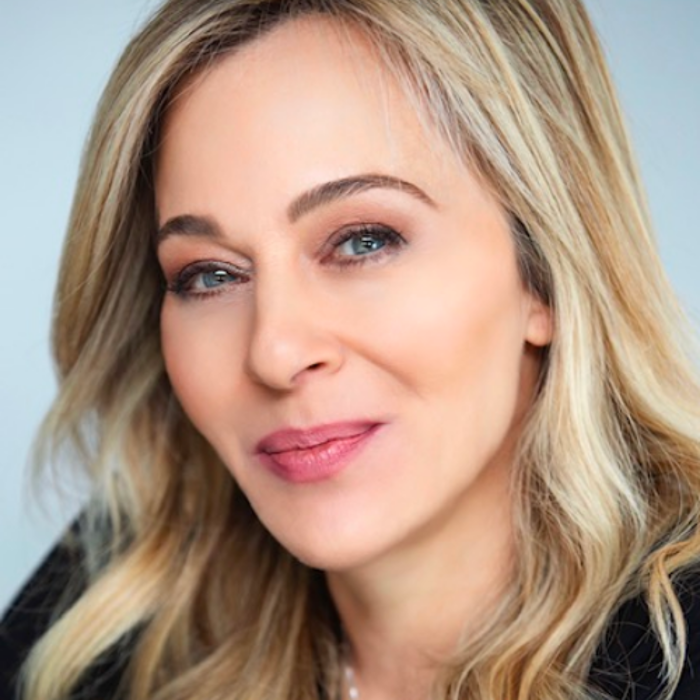 A woman with long blonde hair and blue eyes, smiling softly, wearing a black top.