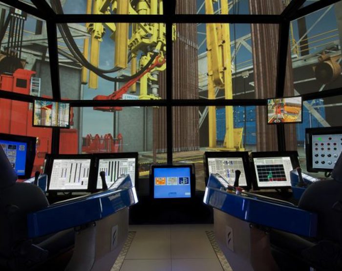 A high-tech control room with multiple monitors and screens displaying various data and machinery. Two ergonomic chairs are positioned in front of the equipment.
